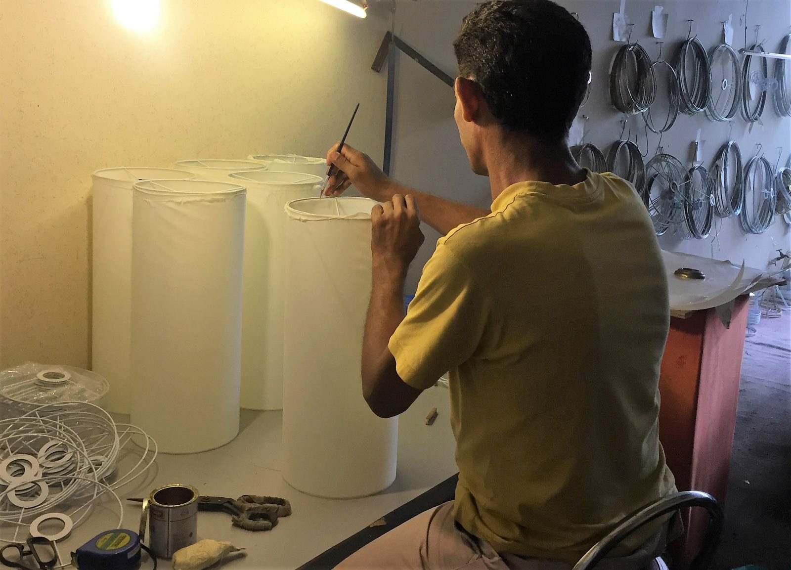 Craftsman hand-finishing the top seam of a cylindrical fabric lampshade